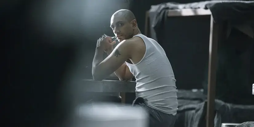 Riz Ahmed in a tank top and grey sweatpants, sitting in Rikers, in The Night Of